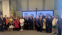 Large group of people standing in front of large screens with Metro 50th anniversary logo.